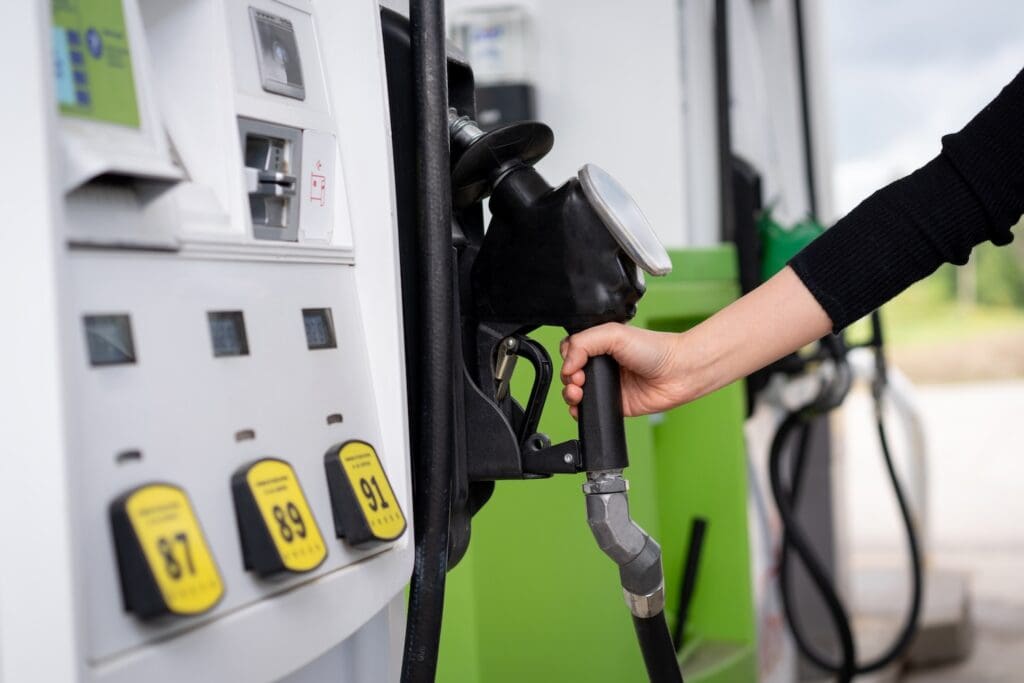 A woman reaches for a gasoline pump nozzle at a fuel station